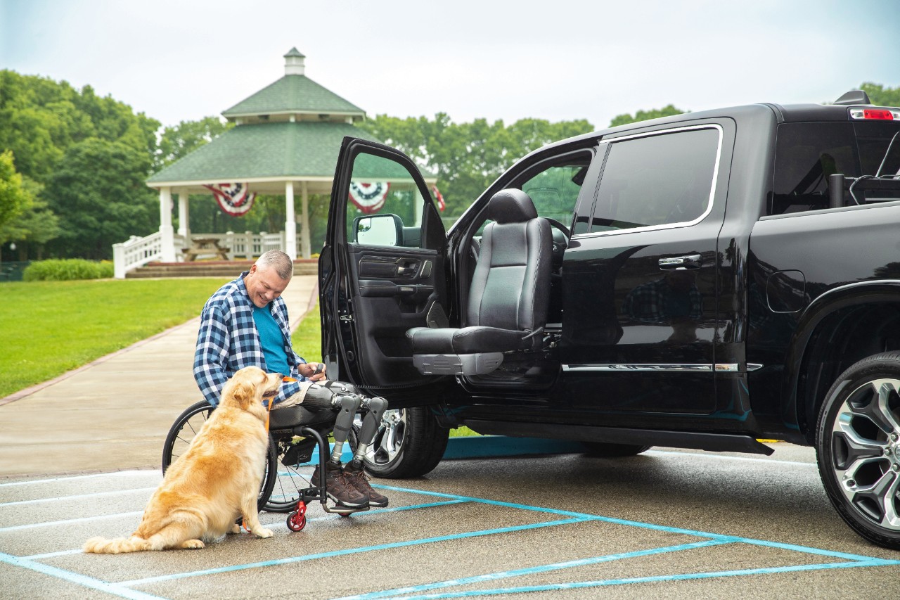 man in wheelchair with dog alongside a truck with accessible seating